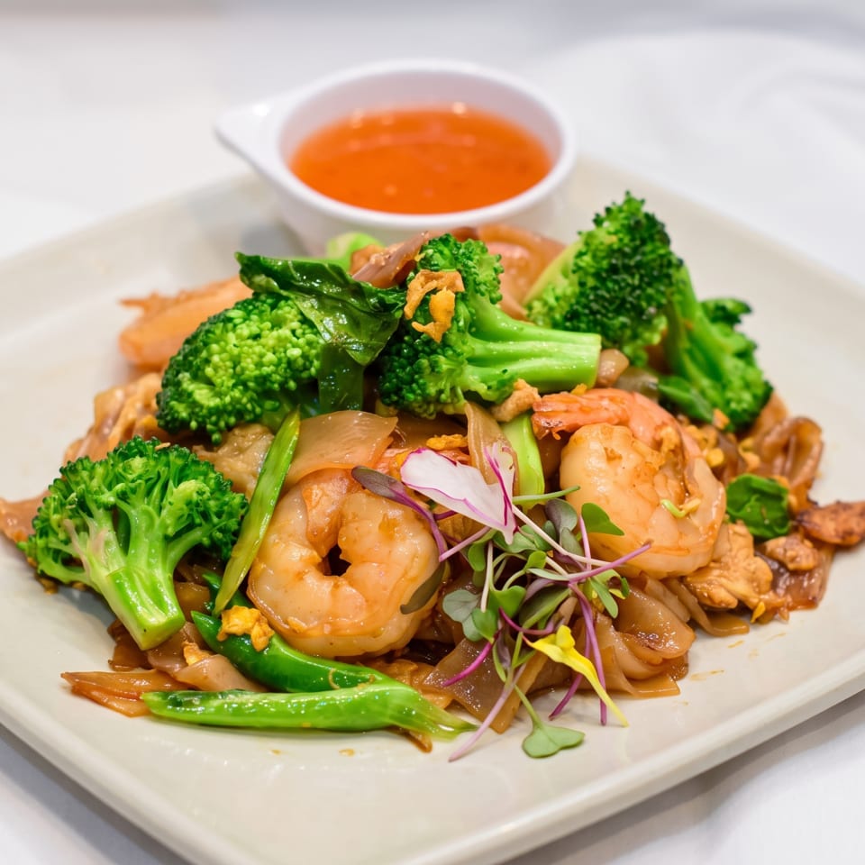 Pad See Ew with shrimp, chicken, broccoli, and green beans, served with a side of sauce.