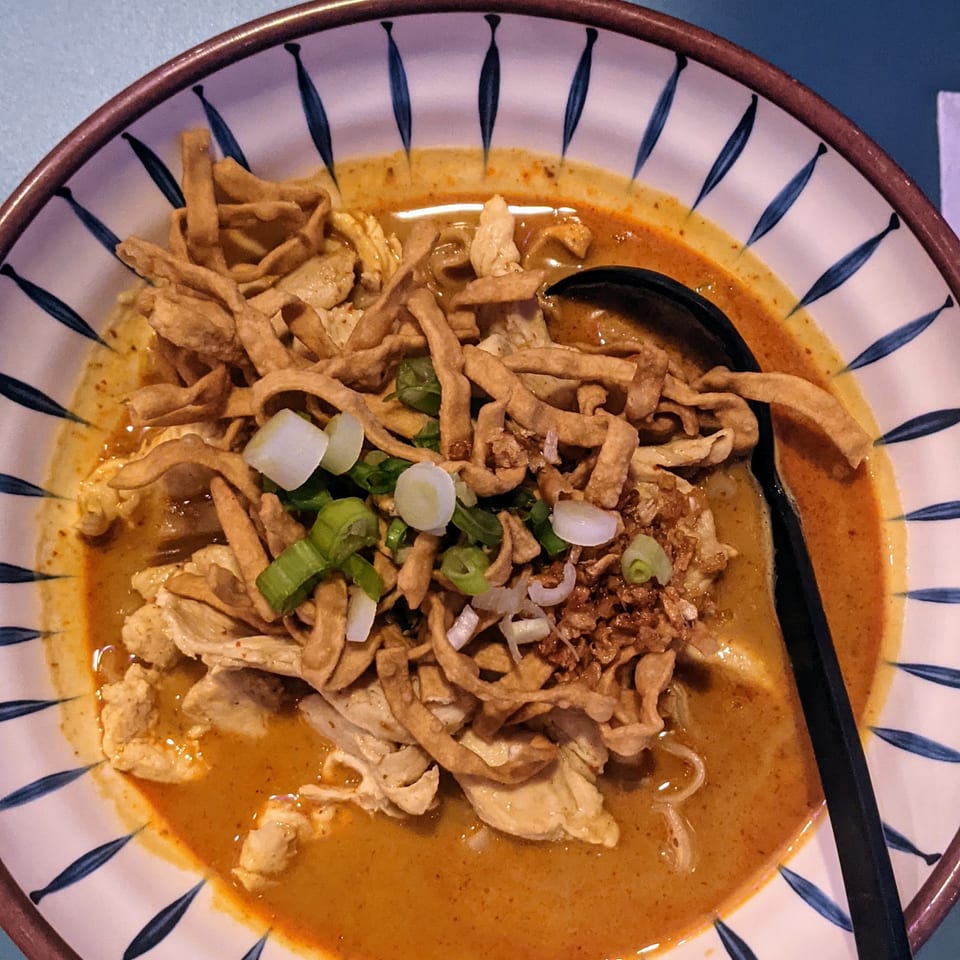 Close-up of a bowl of Khao Soi with chicken, crispy noodles, and green onions.