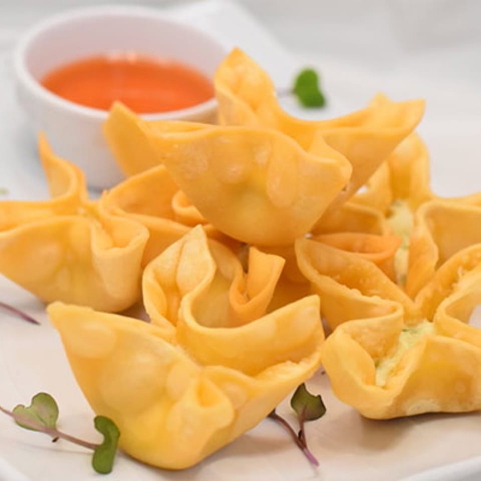 Golden-fried crab rangoon appetizers, garnished with microgreens, and a side of sweet chili dipping sauce.